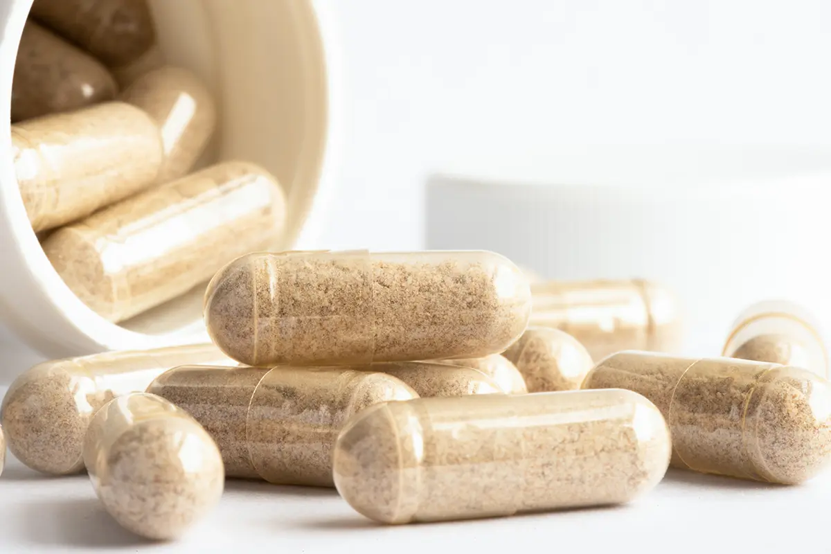 Natural health supplement capsules spilling onto a white counter top from an upturned bottle
